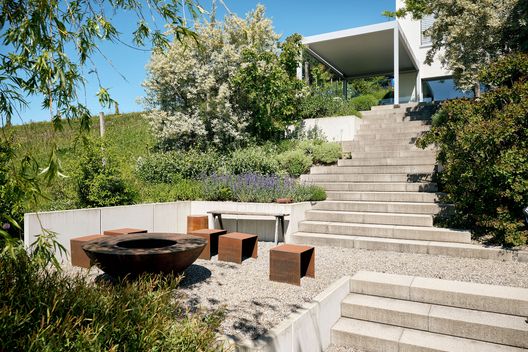 Moderner Hanggarten mit Terrasse, Sitzplatz, Bäumen und Aussicht auf die umliegende Landschaft