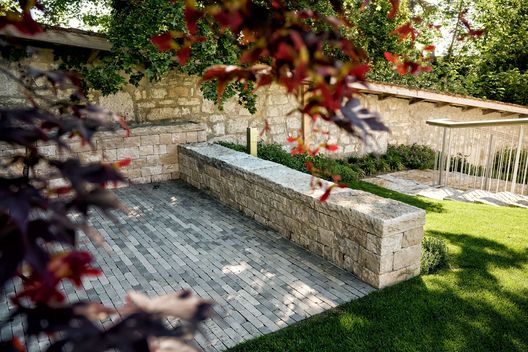 Natursteinsitzplatz mit Kalksteinmauer, Pflästerung und angrenzender Rasenfläche