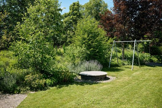 Gartenanlage mit Rasenfläche, Schaukel, Sitzplatz und vielfältiger Bepflanzung aus Stauden und Gehölzen