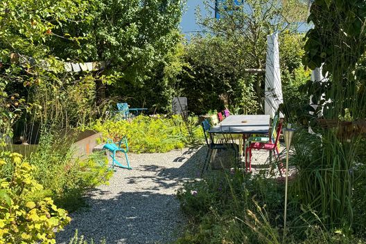 Naturnaher Garten mit Kiesweg, Essplatz im Freien, artenreicher Bepflanzung und nachhaltiger Gartengestaltung.