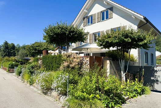 Exklusiver Vorgarten mit Staudenbeeten, formgeschnittenen Bäumen und moderner Gartengestaltung bei einem Einfamilienhaus.