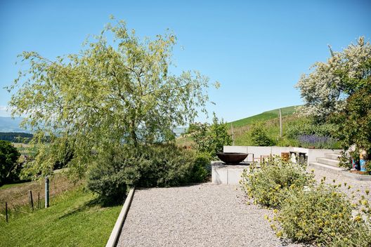 Weitläufiger Hanggarten mit Kiesfläche, Gehölzen, Stauden und Feuerring mit Blick ins Grüne