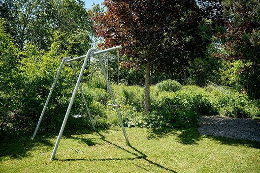 Schaukel auf der Rasenfläche mit angrenzender Stauden- und Gräserbepflanzung im Garten eines Mehrfamilienhauses