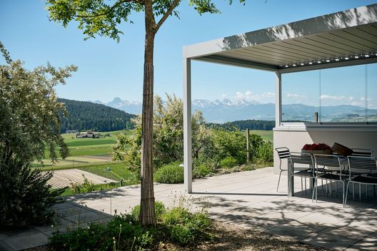 Terrassierter Gartenbereich mit Sitzplatz, Bäumen und vielfältiger Bepflanzung am modernen Wohnhaus
