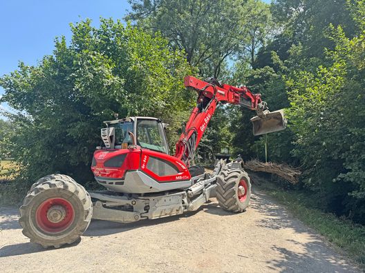 Roter Bagger transportiert gebündelte Äste für die Bachsanierung in Jegenstorf.