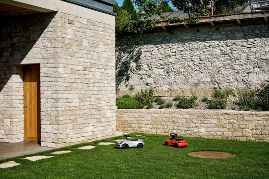 Natursteinfassade mit Rasenfläche, Kalksteinmauern und Spielbereich im Privatgarten