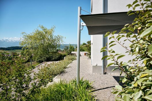 Kiesweg entlang des Hauses mit bepflanztem Hanggarten und Aussicht auf die Landschaft