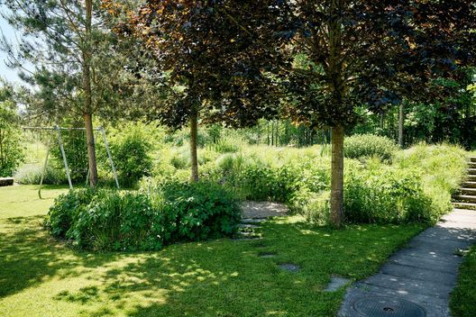 Sanierte Gartenanlage beim Mehrfamilienhaus mit Rasenfläche, Bäumen, Stauden und Spielbereich