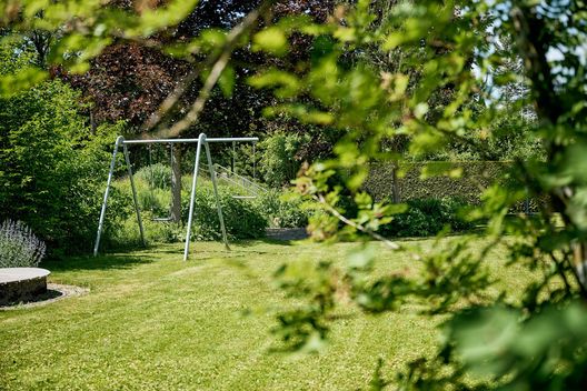 Spielbereich mit Schaukel in einer naturnah bepflanzten Gartenanlage eines Mehrfamilienhauses