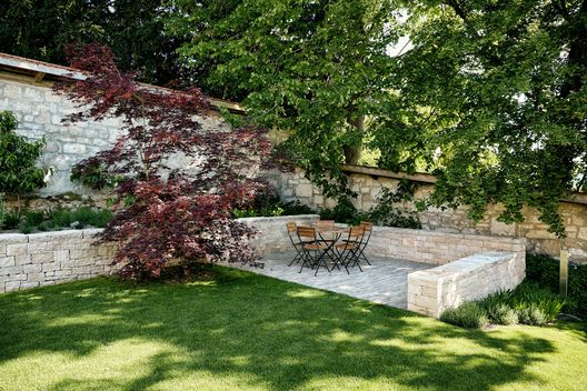 Sitzplatz mit Kalksteinmauer, Natursteinpflästerung und alter Gartenmauer im Hintergrund